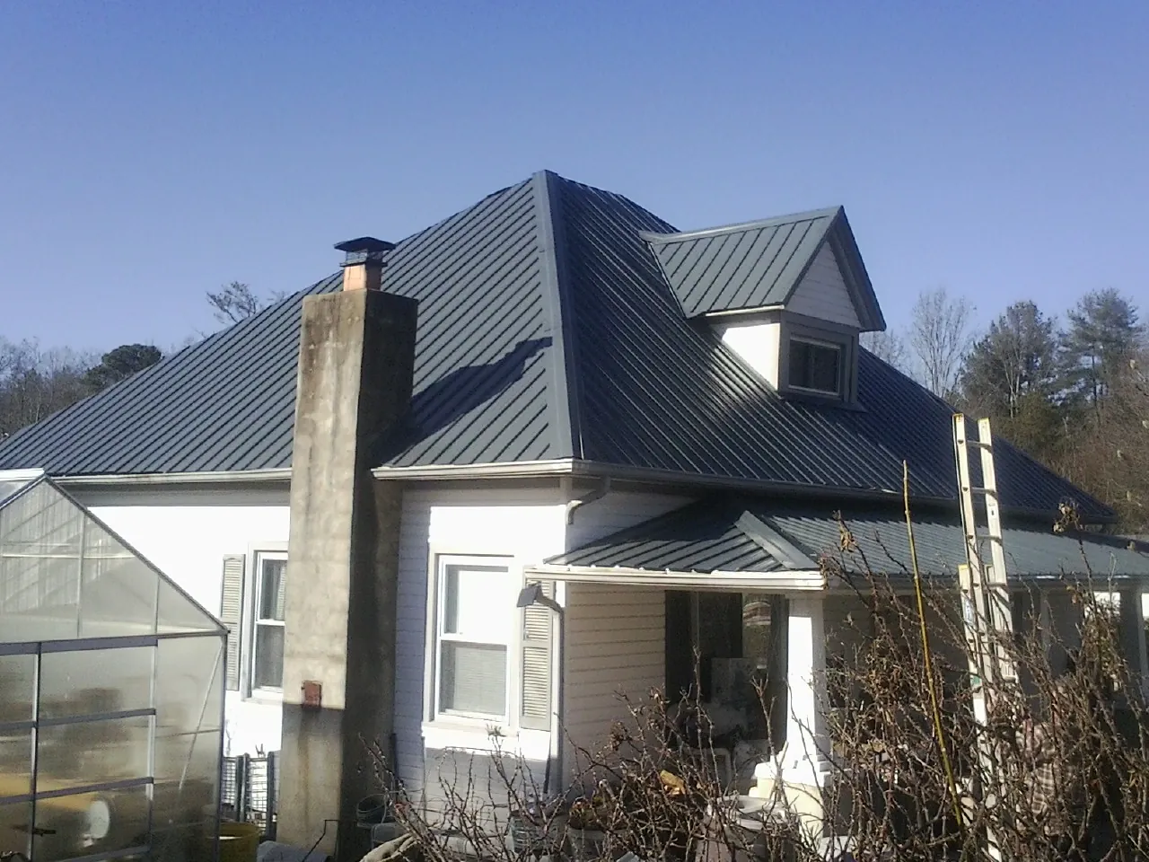 Dark blue standing seam metal roof on a white farmhouse with dormer — Slate & Tile Roof Repair by Roofing Brothers in Pinewood