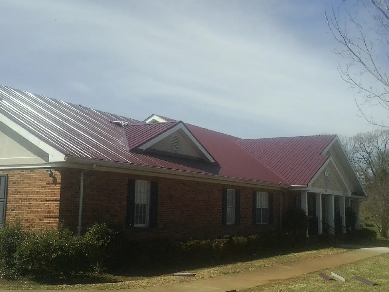 Red metal roof with gabled entries on a long brick building, from a Hail Damage Roof Repair job in Pinewood
