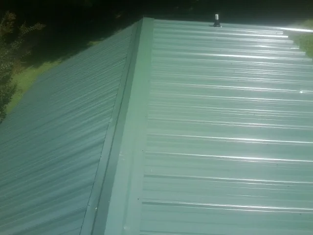 New green metal panels meeting at the ridge of a roof — Flat Roof Repair work by our crew in Pinewood