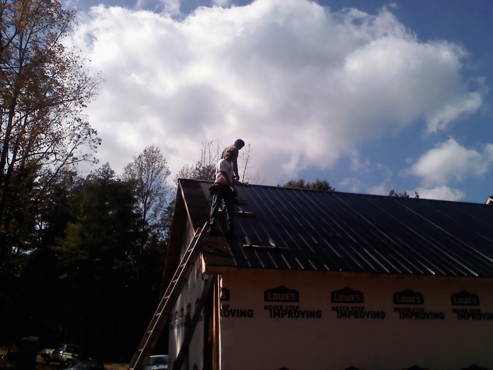 Roofer fastening dark metal panels high against a cloudy sky, from a Roof Inspection job in Pinewood