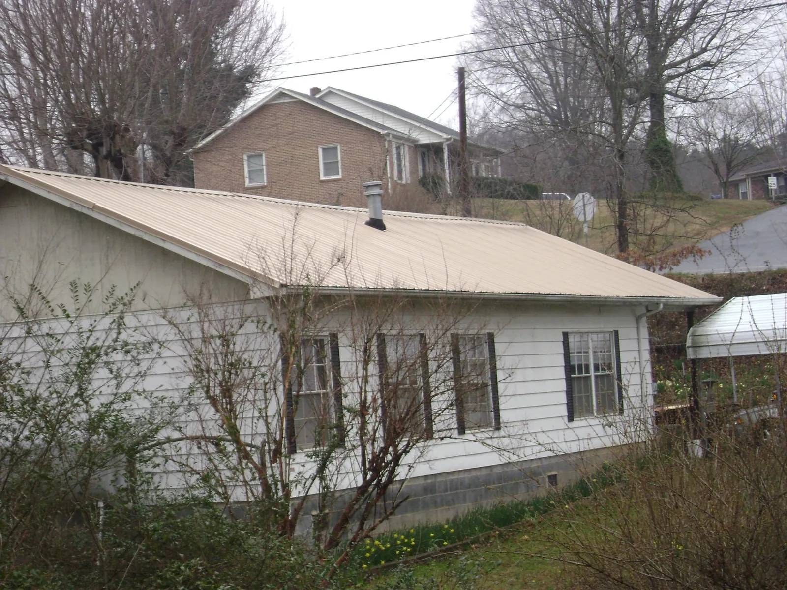 Tan metal roof on a white sided house set into a hillside — Commercial Roofing by Roofing Brothers in Pinewood